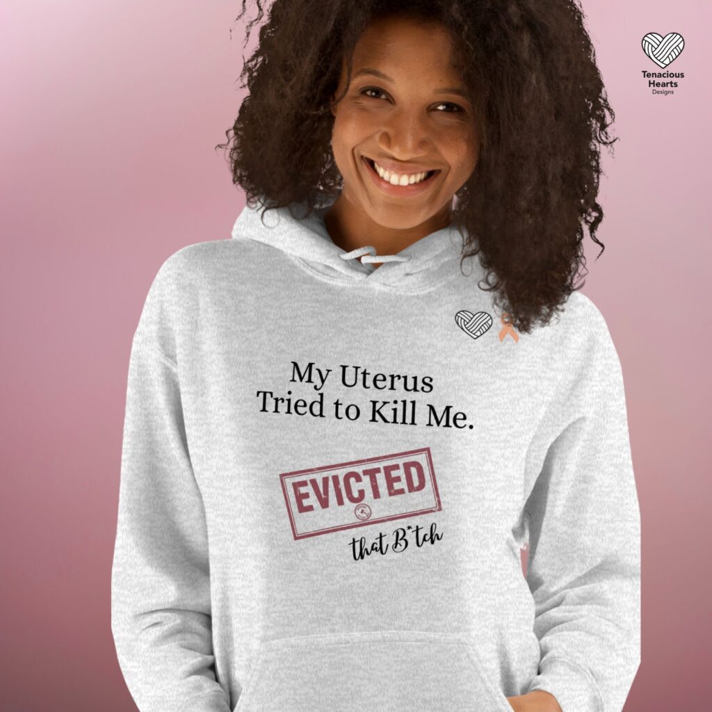 Ash gray hoodie with endometrial cancer survivor message My Uterus Tried to Kill Me EVICTED with peach ribbon on pink background