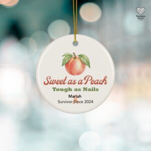 Founder's personalized endometrial cancer survivor ornament featuring "Sweet as a Peach, Tough as Nails" with Mariah's name and 2024 survivor date, hanging against holiday lights background